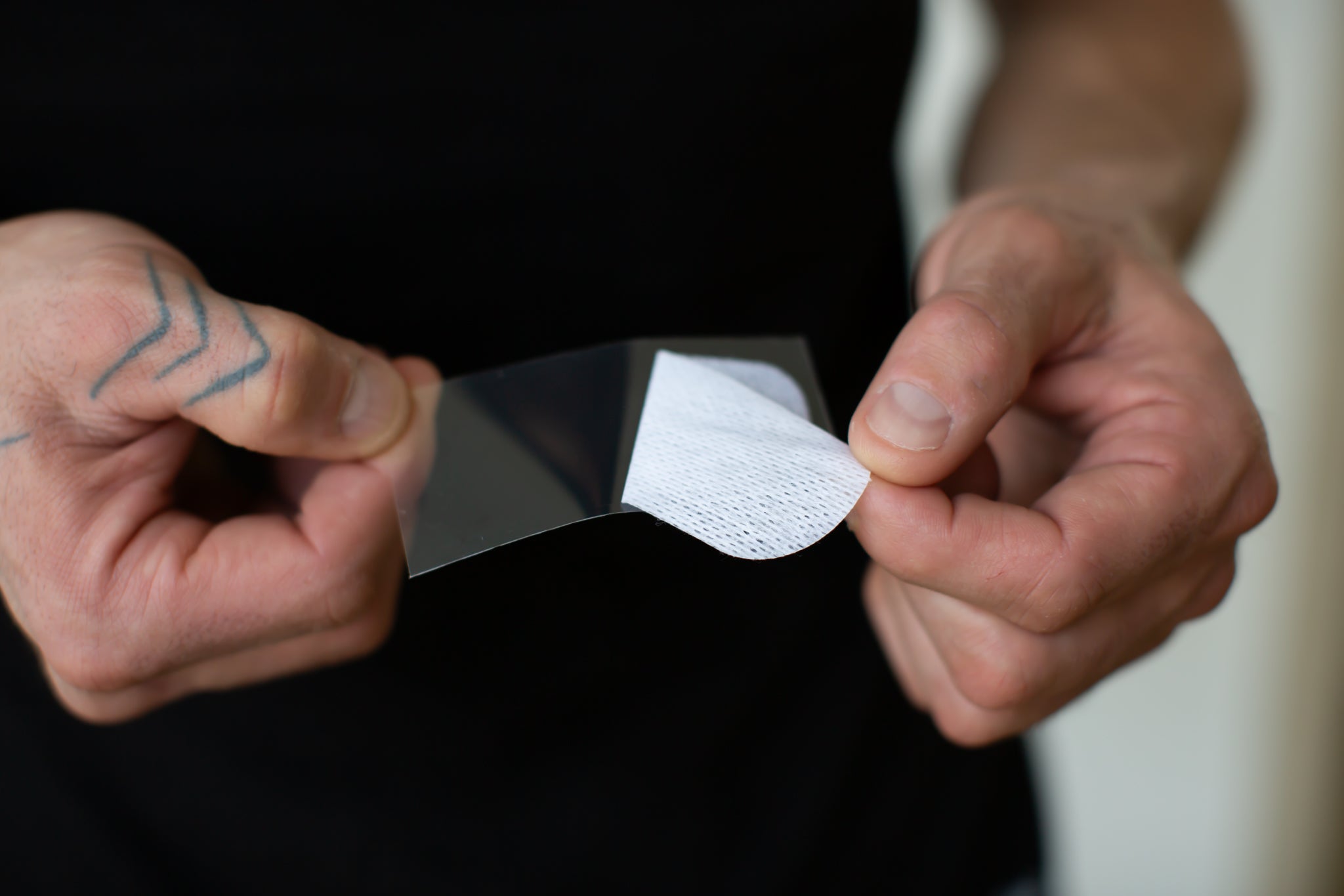 model holding a single non-vented oi tape mouth tape strip and peeling the backing off with his fingers